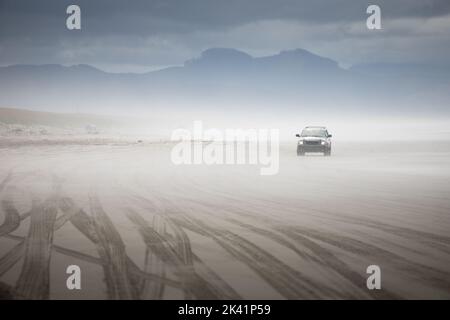 Reifenspuren im Sand von Lastwagen, die am Strand unterwegs waren, mit einem SUV, der aus dem Nebel kam Stockfoto