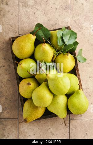 Birnen. Frische süße Bio-Birnen mit Blättern in Holzkiste oder Korb auf alten Steinfliesen Hintergrund. Herbsternte der Früchte. Draufsicht. Hintergrund der Speisen Stockfoto