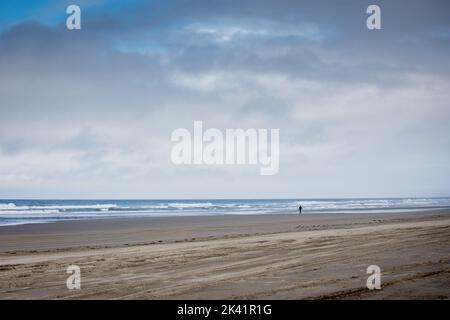 Eine einsame Person, die an einem einsamen Sandstrand entlang läuft Stockfoto