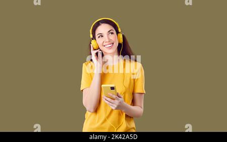 Lächelnde Frau, die ihr Mobiltelefon mit einer Wiedergabeliste hält und ihre Lieblingsmusik über Kopfhörer hört. Stockfoto