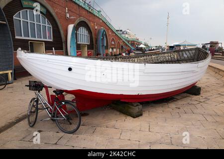 Ein altes offenes Fischerboot (das zur Sicherung eines Fahrrads verwendet wird), eine Museumsausstellung vor dem Brighton Fishing Museum, East Sussex. VEREINIGTES KÖNIGREICH. (131) Stockfoto