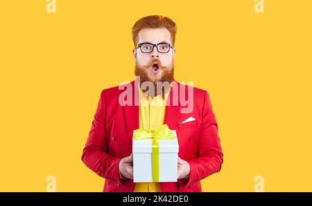 Lustiger molliger Rothaariger bärtiger junger Mann in roter Jacke und Brille bekommt ein tolles Geschenk Stockfoto