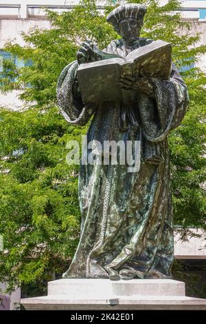 Rotterdam, Niederlande - 11. Juli 2022: Nahaufnahme einer grünlichen bronzenen Erasmus-Statue mit grünem Laub auf dem Grotekerkplein. Stockfoto