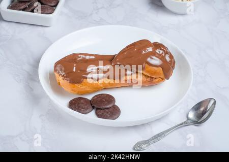 Appetitliches eclair, bedeckt mit Schokolade auf einem weißen Servierteller auf grauem Hintergrund Stockfoto