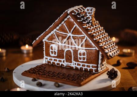 Lebkuchenhaus auf einem hölzernen Hintergrund in stimmungsvollen weihnachtlichen Rahmen. Feiertagsstimmung, Lichter und Kerzen. Wintersaison. Dekoriertes Dessert und Spiel Stockfoto