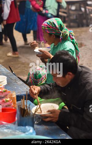 Frau und Mann aus vietnamesischen Volksgruppen tragen traditionelle Kleidung und essen in der Markthalle der Gemeinde Meo Vac, Vietnam. Stockfoto