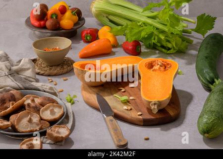 Herbstgemüse auf einer Küchenarbeitsfläche angeordnet, während eine Kürbissuppe zubereitet wird. Stockfoto