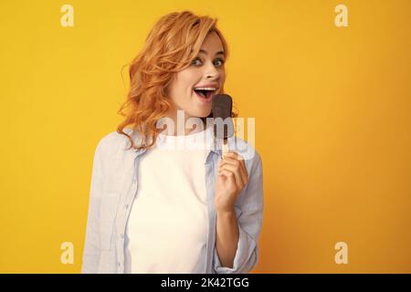 Sommerkonzept. Froh positive Frau hält leckere gefrorene Eis, genießt es, köstliche kalte Dessert essen, Posen auf gelbem Hintergrund, fühlt sich glücklich Stockfoto