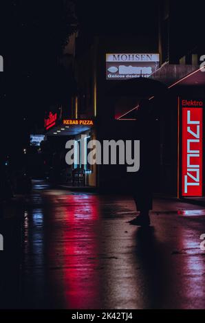Neon Nachtleben auf den Straßen. Helle Neonschilder, die auf der nassen/regnerischen Straße spiegeln. Neonschilder, die die Silhouette einer Person schaffen. Stockfoto