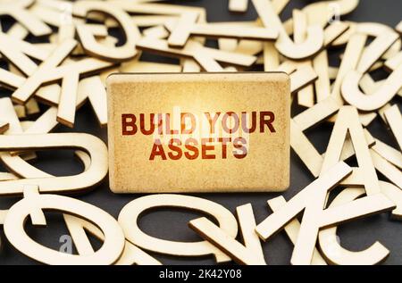 Bildungskonzept. Unter den hölzernen Buchstaben ist ein Schild mit der Aufschrift - bauen Sie Ihre Vermögenswerte Stockfoto