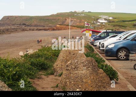 Widemouth Bay Blick nach Norden vom Parkplatz, zeigt die Fronten einer Reihe von Autos, die RLNI Hütte die Klippen und Wanderer am Strand Stockfoto