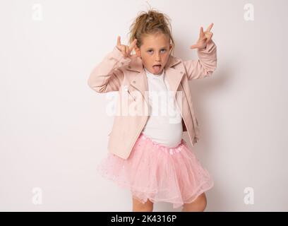 Portrait eines aufgeregt staunenden kleinen Mädchens in weißem T-Shirt, das mit Rock-Singen und offenem Mund die Kamera anschaut und vor Aufregung schreit. Studio im Innenbereich Stockfoto