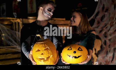 Datum im Stil von Halloween-Party, Nacht, Dämmerung, in den Strahlen des Lichts, Kerl mit einem Mädchen in Kostümen gekleidet und mit einem schrecklichen Make-up halten zwei große Halloween Kürbisse. Hochwertige Fotos Stockfoto