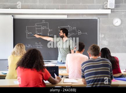 Junger männlicher Lehrer, der an der Tafel erklärt Stockfoto