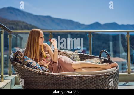 Portrait einer wunderschönen Frau in einem wunderschönen Kleid, die auf einer Terrasse sitzt und Erdbeere isst Stockfoto