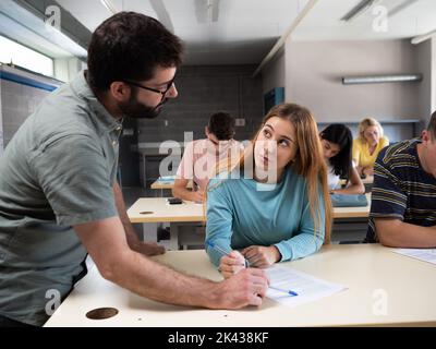 Männlicher Lehrer, der eine junge Schülerin in der Klasse berät. Stockfoto