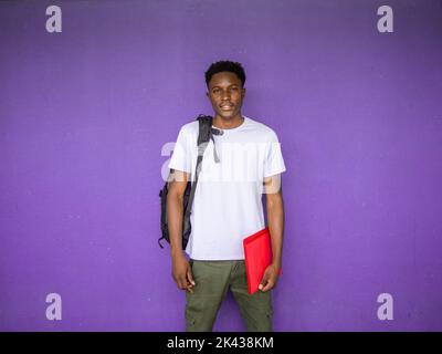 Porträt einer jungen afroamerikanischen Studentin, die mit einem Rucksack und einem Ordner auf die Kamera schaut. Zurück in die Schule, High School, Universität Stockfoto