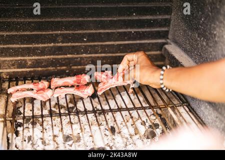 Hände eines lateinischen Mannes, der Schweinerippen auf den Grill legt Stockfoto