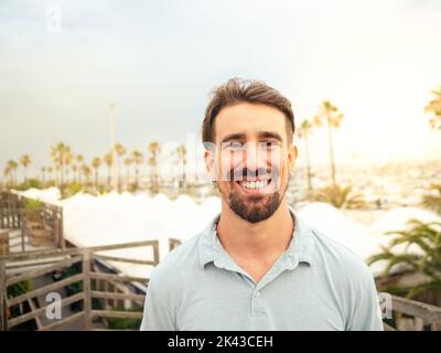 Lächelnder junger spanier, der bei einem Sonnenuntergang mit Palmen auf die Kamera schaut Stockfoto