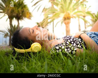 afroamerikanische Frau hört Musik, die im Park auf dem Rasen liegt Stockfoto