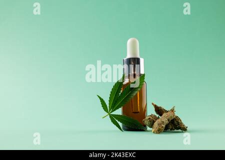 Bild einer Flasche CBD-Öl und getrockneten Marihuana-Blättern auf grüner Oberfläche Stockfoto
