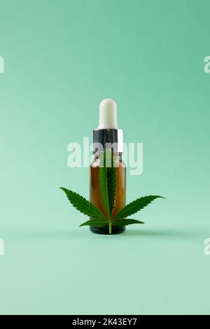 Vertikale Abbildung einer Flasche CBD-Öl und Marihuana-Blatt auf grüner Oberfläche Stockfoto