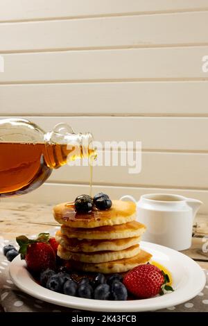 Vertikale Abbildung von Ahornsirup Gießen auf Stapel von Pfannkuchen mit Heidelbeeren, mit Kopierraum Stockfoto