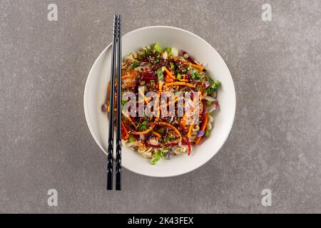 Blick von oben auf den asiatischen Wok-Rührbraten und Essstäbchen auf grauem Hintergrund Stockfoto