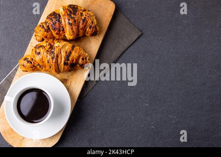 Bild von Croissants und Kaffee auf Holzbrett auf dunkelgrauer Oberfläche Stockfoto