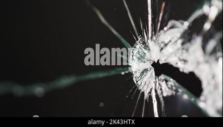Nahaufnahme einer zerbrochenen, rissenen Glasscheibe mit Loch, auf schwarzem Hintergrund mit Platz zum Kopieren Stockfoto