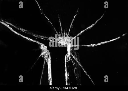 Nahaufnahme einer zerbrochenen, rissenen Glasscheibe mit Loch auf schwarzem Hintergrund Stockfoto