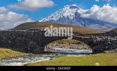 Cotopaxi, der zweithöchste aktive Vocano der Welt und der Pita-Fluss, der an seinen Hängen ansteigt und unter der alten Steinbrücke von La Merced fließt Stockfoto