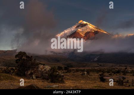 Cotopaxi Vulkan in der Dämmerung. Der Vollmond geht auf der linken Seite auf und beleuchtet den Vulkan, während das orangefarbene Licht der untergehenden Sonne den erhellt Stockfoto