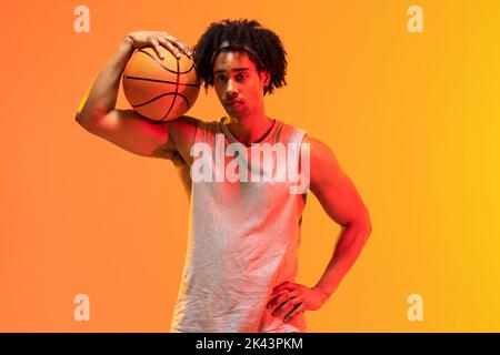 Bild von biracial Basketballspieler mit Basketball auf orange bis gelb Hintergrund Stockfoto