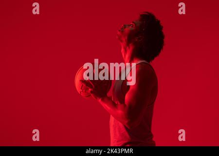 Bild von Biracial Basketballspieler mit Basketball auf neonrotem Hintergrund Stockfoto