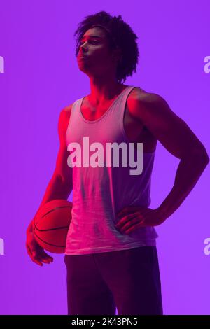 Bild von biracial Basketballspieler mit Basketball auf neon-lila Hintergrund Stockfoto