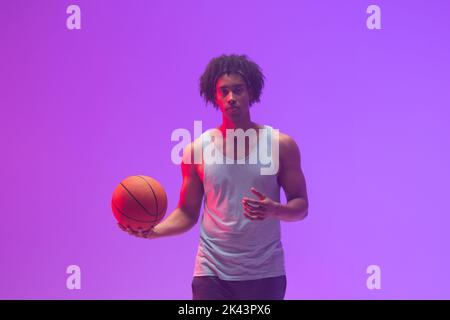 Bild von biracial Basketballspieler mit Basketball auf neon-lila Hintergrund Stockfoto