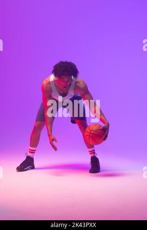 Bild von biracial Basketballspieler mit Basketball auf neon-lila Hintergrund Stockfoto