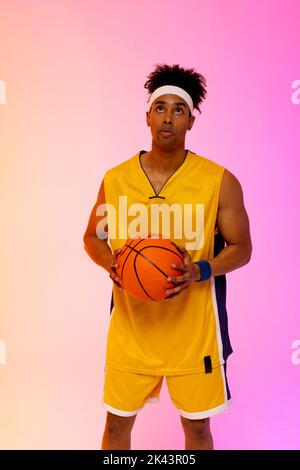 Bild von biracial Basketballspieler mit Basketball auf rosa bis orange Hintergrund Stockfoto