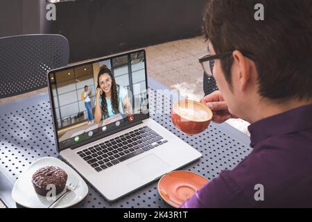 Multirassischer Geschäftsmann, der mit einem Kollegen auf einer Videocall über einem Laptop diskutiert, während er Kaffee trinkt Stockfoto