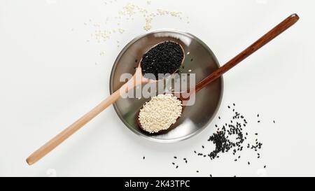 Schwarze und weiße Sesamsamen in einem Holzlöffel. Auf weißem Tisch Stockfoto