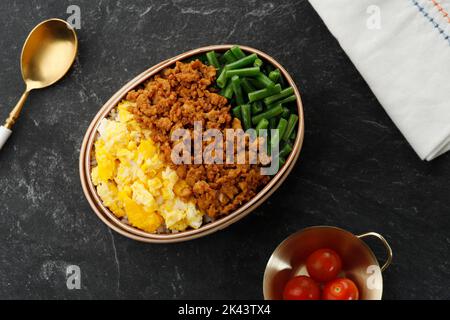 Dreifarbige Lunchbox mit japanischem Reis, Rührei, gehacktes Huhn, gekochte französische Bohnen und Scramble-Eier. Sanshoku Lunchbox Stockfoto