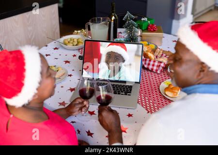 afroamerikanische Großeltern in santa Hüte auf weihnachten Laptop-Videoanruf mit Enkel. weihnachten, Festlichkeit und Kommunikationstechnik. Stockfoto