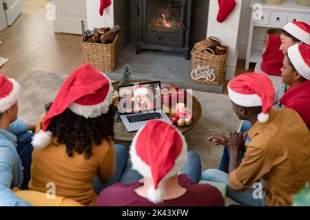 Biracial Freunde in santa Hüte auf Laptop weihnachten Videoanruf mit lächelnden Frau. weihnachten, Festlichkeit und Kommunikationstechnik. Stockfoto