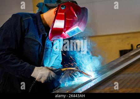 Mitarbeiter mit Maske schneidet Balken mit Heißgasabschneider im Werk Stockfoto