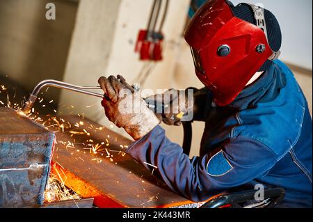 Schweißer in Maske schneidet Stahlträger mit Schneiderblowrohr in der Werkstatt Stockfoto