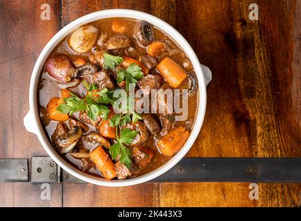 Weiße Keramikschale mit köstlichem französischem Rindereintopf, Boeuf Bourguignon, auf rustikalem Holztisch. Stockfoto