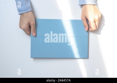 Ein Tablet in einer blauen Hülle auf einem weißen Schreibtisch. Die Lichter einer Sonne. Die Hände des Mädchens halten ein Tablet. Draufsicht Stockfoto