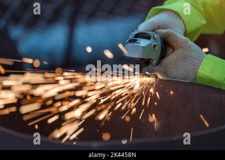 Nahaufnahme eines Industriearbeiters mit Winkelschleifer und Schneiden eines Metallrohrs. Arbeiter in Sicherheit Uniform und Harthut Herstellung Metallstrukturen. Stockfoto