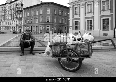 Poznan, Polen - Ein Mann, der Flaschen für seinen Lebensunterhalt sammelt und auf einer Wand auf dem Kolegiacki-Platz sitzt. Stockfoto